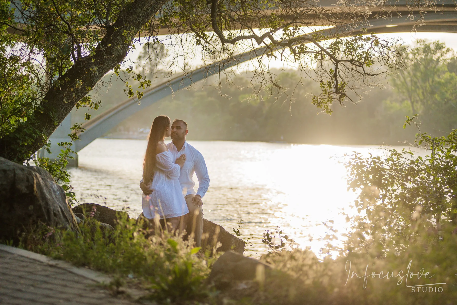 An engaged couple beneath an arching tree by the river