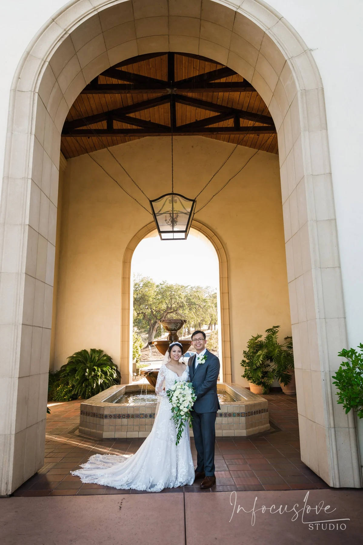 Newlyweds together beneath a sunlit stone archway